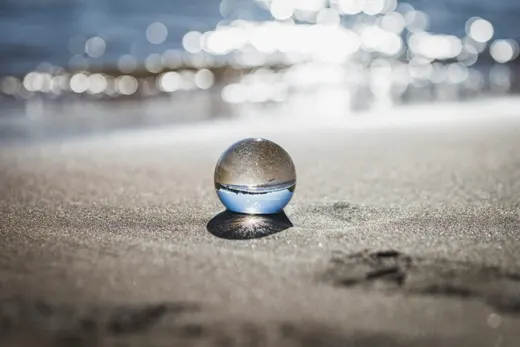 Glaskugel liegt am Sandstrand vor dem unscharfen Lichtspiel des Meeres